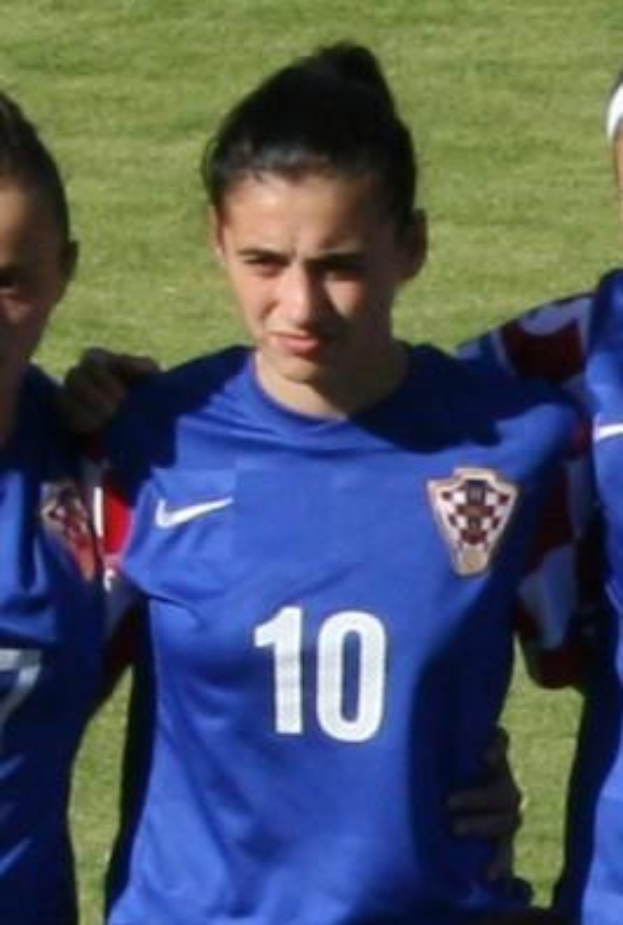 Drei Frauen aus dem Nationalteam der kroatischen Frauen stehen auf einem Fußballfeld in blauen T-Shirts, eine trägt ein weißes Stirnband, vor grünem Gras.