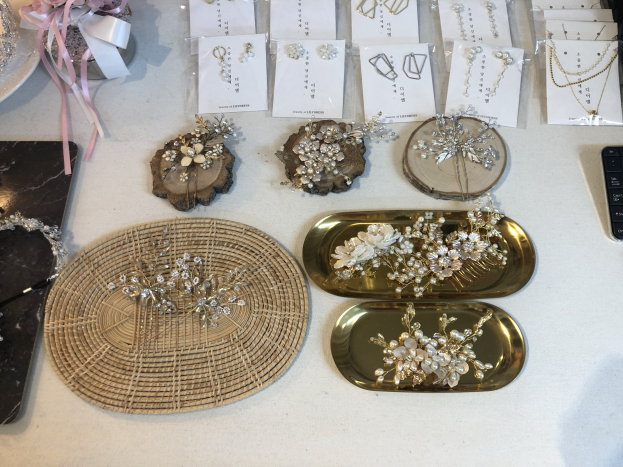 Ein unordentlicher Tisch in einem Brautmodengeschäft, auf dem verschiedene Schmuckstücke, Papiere, eine Tastatur und ein Mobiltelefon sowie andere Gegenstände liegen.