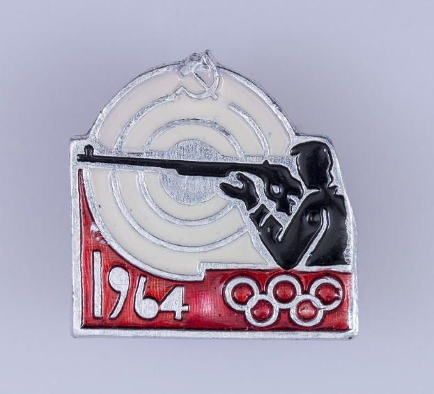 Olympische Spiele-Badge mit einem Mann in rot-weiß gestreiftem Hemd und schwarzem Hut, der auf ein Ziel schießt, mit dem Text "1964 Olympische Spiele", vor einem hellblauen Himmel mit weißen Wolken.