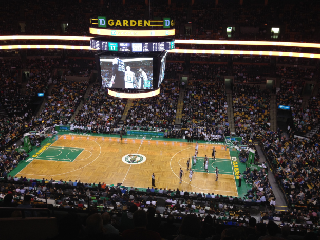 Basketballspiel im Gange in der TD Garden, mit Zuschauern auf den Rängen und einem Scoreboard oben auf dem Court.