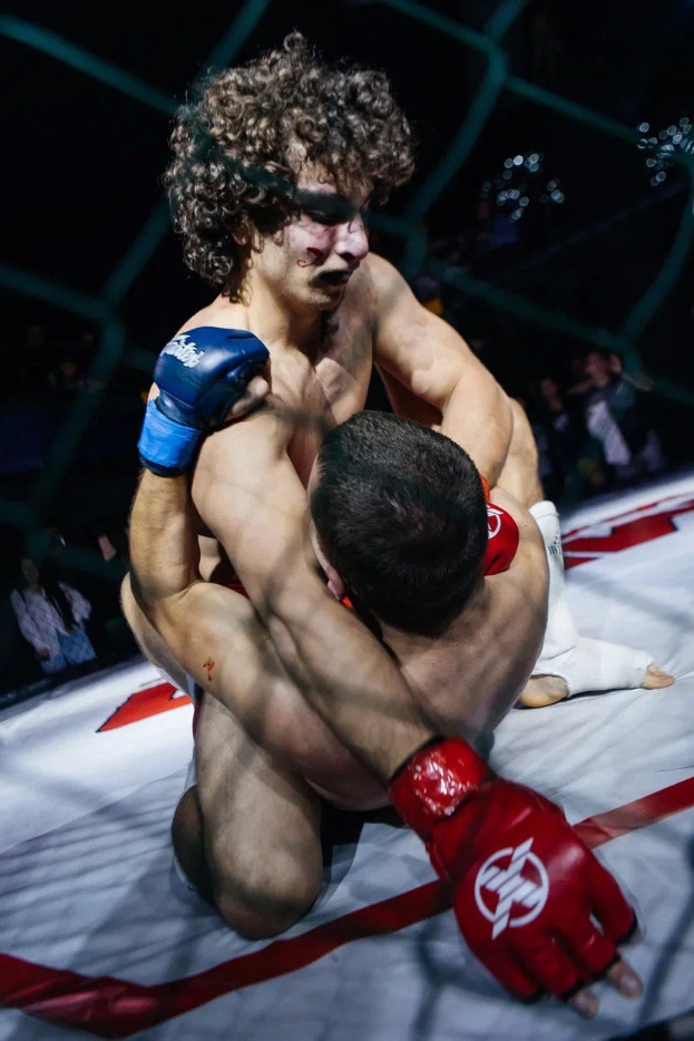 Zwei Männer in einem MMA-Ring liefern sich einen Kampf, wobei einer einen Tritt gegen den anderen landet.