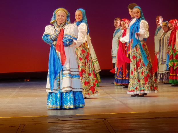 Eine Gruppe von Menschen in bunten, detaillierten traditionellen ukrainischen Kostümen lächelt fröhlich auf einer Bühne.