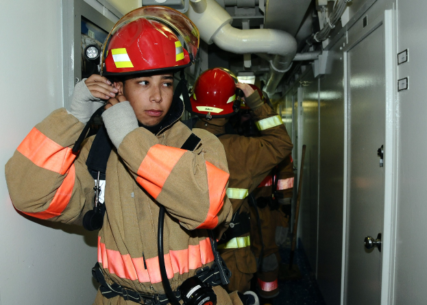 Firefighters in uniform standing in a room with pipes and equipment during a training exercise.