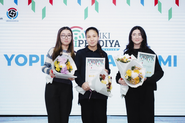 Drei Frauen mit Blumensträußen und Urkunden auf einer Bühne mit einem "Yopi Diya Awards 2019"-Plakat im Hintergrund.