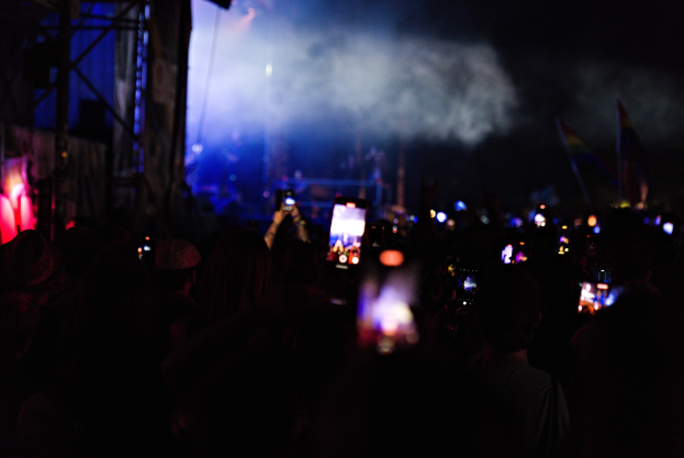 Eine Menge bei einem Konzert hält beleuchtete Handys unter der Bühnenbeleuchtung mit Rauch im Hintergrund hoch.