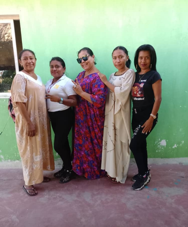 Group of women standing in front of a green wall with a window on the left, participating in an International Women's Day event.