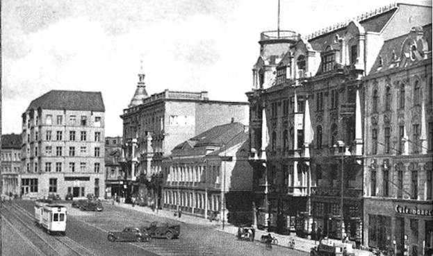 Ein Schwarz-Weiß-Foto einer Stadtstraße in Stuttgart, Deutschland, circa 1900, mit Fahrzeugen, Gebäuden mit Fenstern, Laternen und einem bewölkten Himmel.