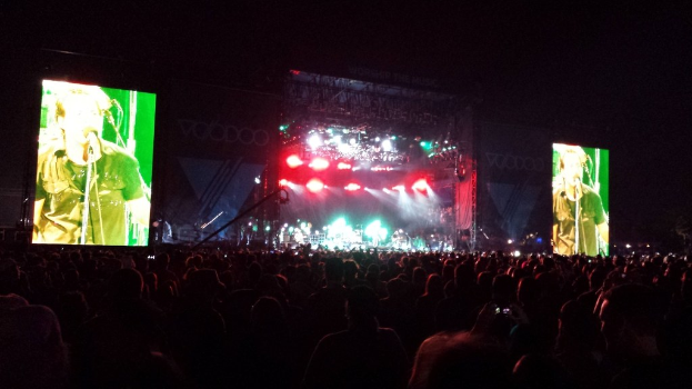 Konzerthalle mit einer Menge unten, flankiert von großen Bildschirmen links und rechts.