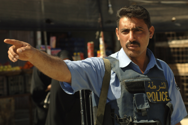 Polizeibeamter in Uniform, der eine Waffe hält, während er vor einem Geschäft steht, mit unscharfen Hintergrundfiguren und -gegenständen.