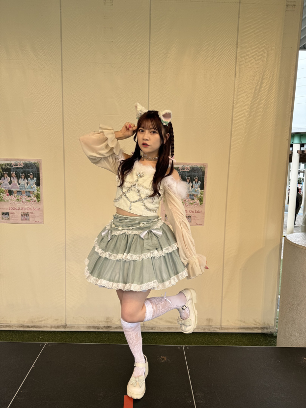 Frau auf einer Bühne bei einem Cosplay-Event, neben einer Wand mit Event-Plakaten, mit einer Säule und einem Gebäude auf der rechten Seite.