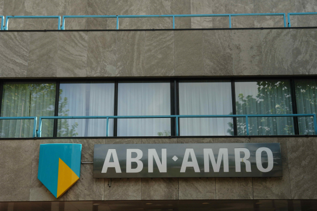 Außenansicht eines ABN AMRO-Gebäudes mit einer Tafel, einer Schautafel, die es als Hauptsitz angibt, Geländern und Vorhangglasfenstern, die auf eine EU-Strafe von 1,5 Milliarden Euro verweisen.