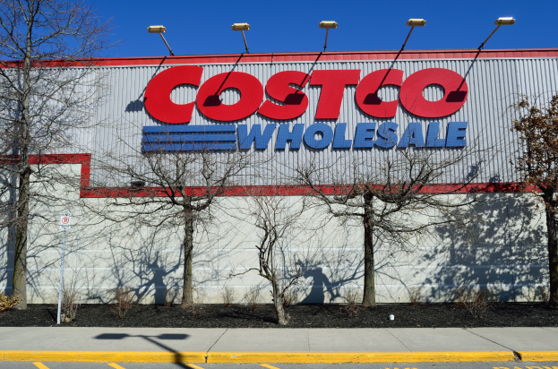 Außenansicht eines Costco Wholesale-Geschäfts mit einer Seite, umgeben von Bäumen, Pflanzen, einer Straße und beleuchtet von Lampen unter einem sichtbaren Himmel.