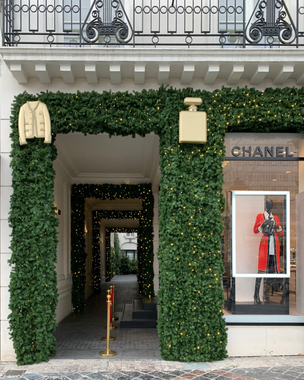 Eintritt in ein Chanel-Geschäft in Paris mit üppiger Vegetation, Beleuchtung und einer Schaufensterpuppe in einem roten Kleid.
