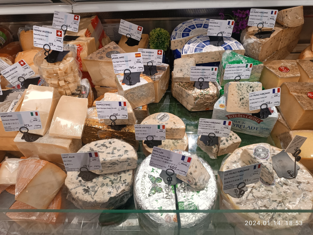 Eine Vitrine voller verschiedener Käsesorten, jede mit einem Preisschild beschriftet und in verschiedenen Formen, Größen und Farben angeordnet.