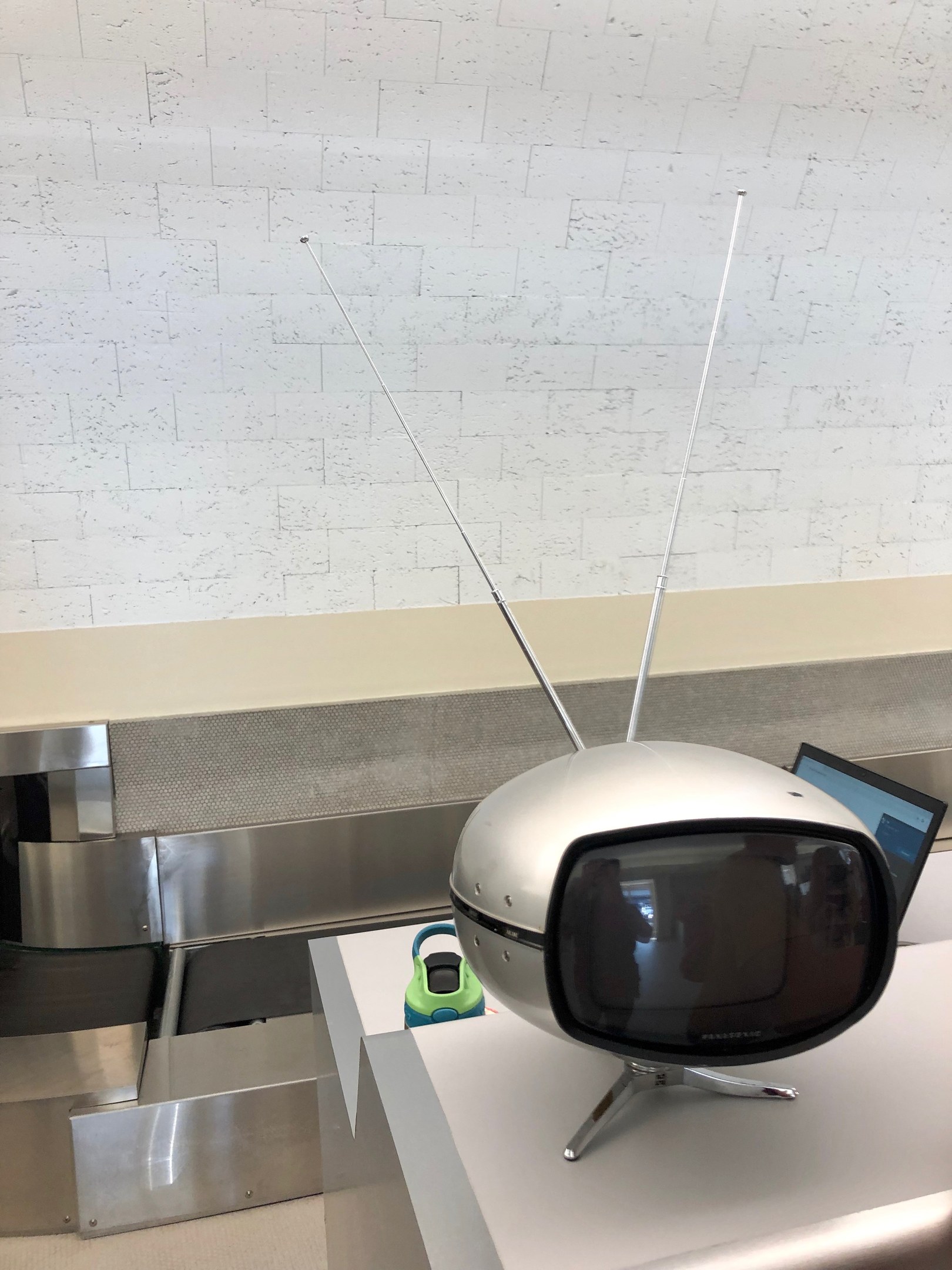 Old television on a counter next to a laptop, with a wall in the background.