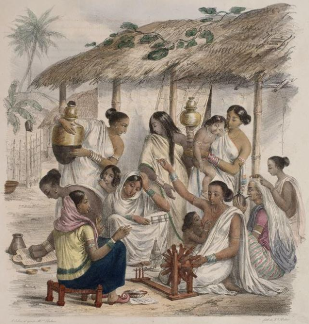 Eine Gruppe von Frauen sitzt um einen Tisch vor einer Hütte, wobei eine einen Topf hält, umgeben von Bäumen, einem Zaun und einem klaren blauen Himmel.