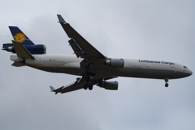 Ein Lufthansa Cargo Boeing 777-300ER im Flug, mit sichtbarem Text an der Seite und weißen Wolken im Hintergrund.