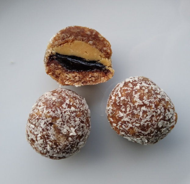 Drei Schokoladen- und Erdnussbutter-Kugeln auf einem weißen Teller, eine mit einem Biss darin, mit Puderzucker bestäubt und die Erdnussbutter-Füllung zeigend.