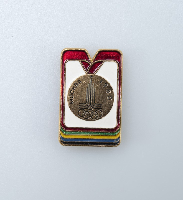 Olympische Medaillenabzeichen von den Olympischen Winterspielen 1980 in Moskau mit einem bunten Design und der Aufschrift "Olympische Spiele" auf einer weißen Oberfläche.