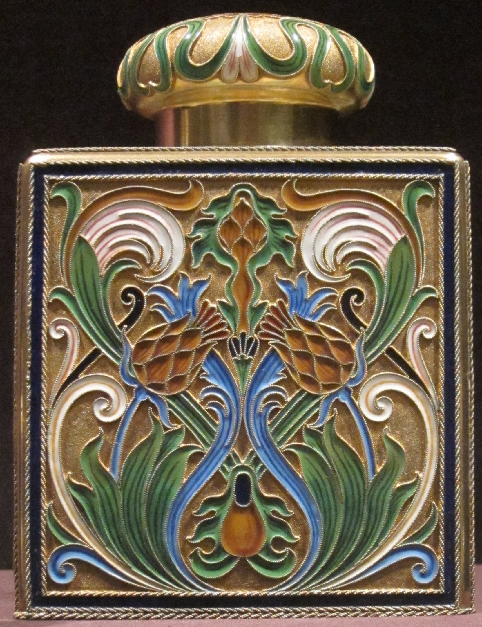 Gold- und Emaille-Parfümflasche mit detaillierten Art-Nouveau-Blumenmustern auf dunklem Hintergrund.