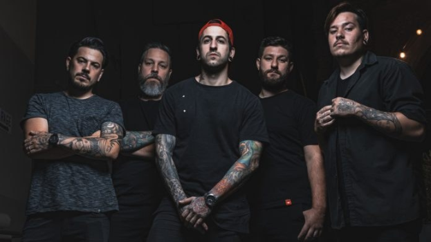 Gruppe von Männern, die in einem dunklen Raum mit rechtsseitiger Beleuchtung stehen und wie in einem Interview für Avenged Sevenfold aussehen.