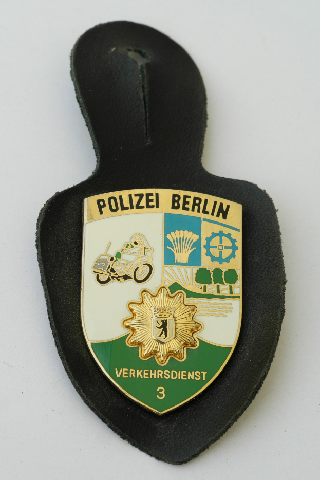 Ein schildförmiges Polize abadge mit 'Polizei Berlin' in fetter schwarzer Schrift auf einem blauen Hintergrund mit einem weißen Stern und Rahmen, das auf einer Oberfläche ruht.