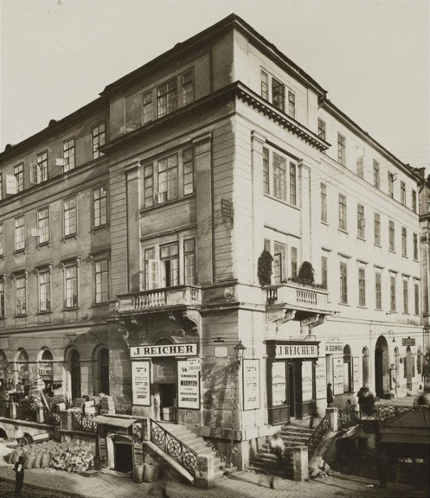 Das J Reicher Hotel in Berlin, ein altes Gebäude mit Fenstern, Treppen mit Geländern, Schildern mit Text und Töpfen mit Pflanzen, mit ein paar Menschen und dem Himmel im Hintergrund.