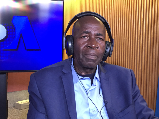 Ein Mann in Anzug und Kopfhörern sitzt vor einem Fernseher und spricht während einer Diskussion über das Internetverbot in Nigeria, mit einer hölzernen Wand im Hintergrund.