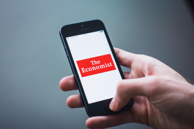 Eine Person hält ein Mobiltelefon in der Hand, auf dem die Economist-App geöffnet ist, mit sichtbarem Text auf dem Bildschirm und einem Teil ihrer Hand.