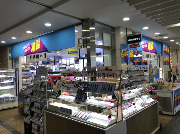 Ladeninneres mit verschiedenen Kosmetika auf Gestellen und Regalen, beleuchtet von Deckenlampen und mit Informationsschildern.