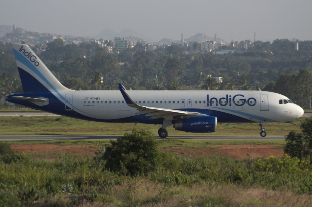 IndiGo Airlines Airbus A320-200 auf der Rollbahn am Mumbai Airport mit Grünflächen, Gebäuden, Türmen, Bergen und Himmel im Hintergrund.