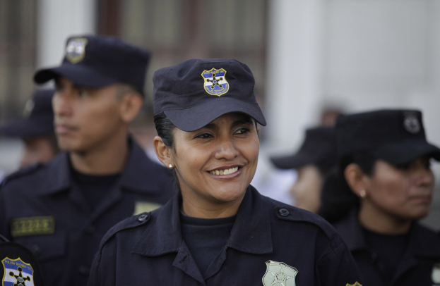 Polizistin in Uniform vor einer Gruppe von Menschen mit Mützen und Abzeichen, mit unscharfem Hintergrund.