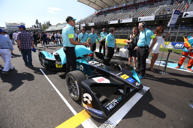 Eine Gruppe von Menschen feiert um ein Formel-E-Rennwagen auf der Strecke, mit einem Stadion voller Zuschauer im Hintergrund unter einem klaren blauen Himmel.
