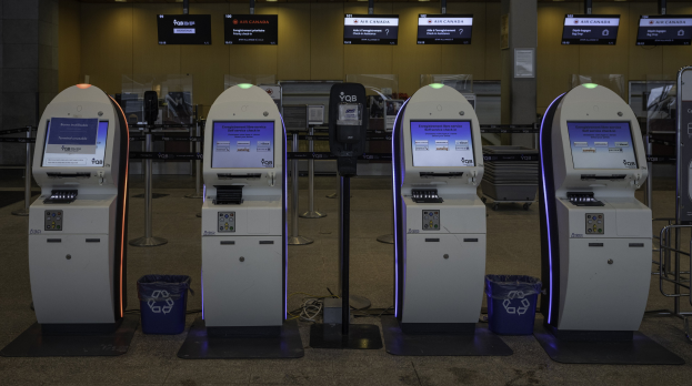Eine Reihe von Geldautomaten auf einem gefliesten Boden mit Mülltonnen, Pfosten, Tafeln mit Text und Lichtern im Hintergrund.