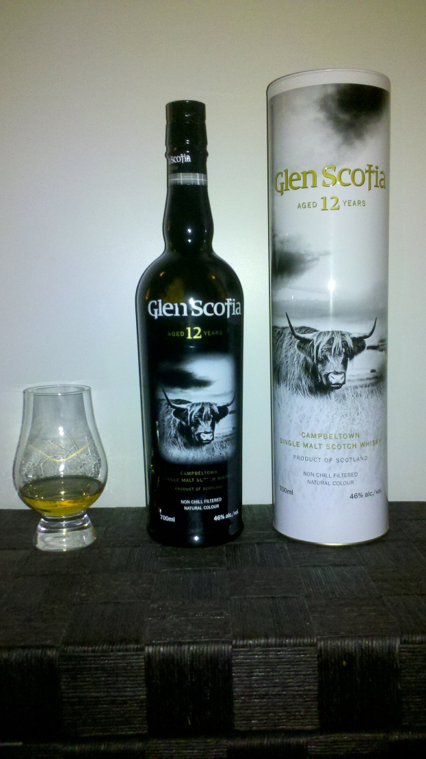 Eine Flasche Glen Scotia 12 Jahre alter Scotch Whisky und ein Glas desselben Whiskys auf einem hellen Holztisch.