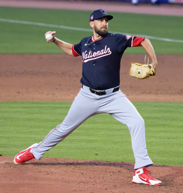 Baseballspieler in Washington-Nationals-Uniform, der auf einem Rasenfeld wirft, mit Zuschauern und World-Series-Related-Signage im Hintergrund.
