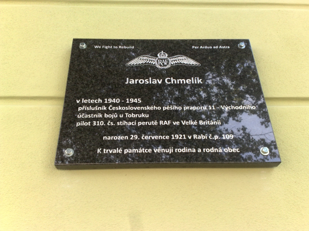 Schwarze Plakette mit weißer 'Jaroslav Chmelik'-Beschriftung und dekorativem Rahmen an einer Gebäudewand.