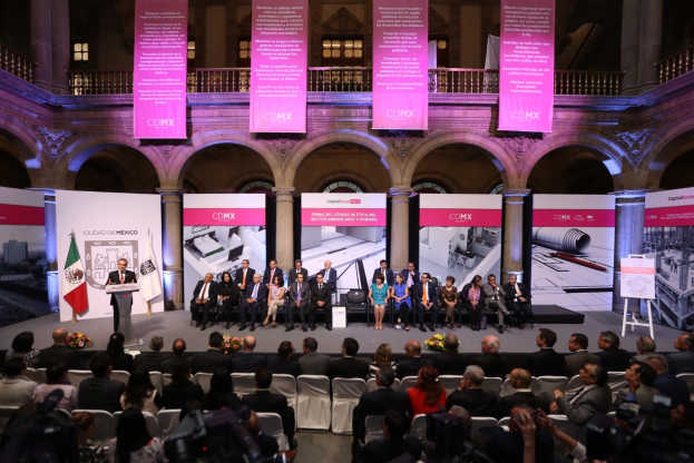 Eine Gruppe von Menschen sitzt auf einer Bühne mit einem Redner am Podium umgeben von Dekorationen während einer Pressekonferenz für CDMX.