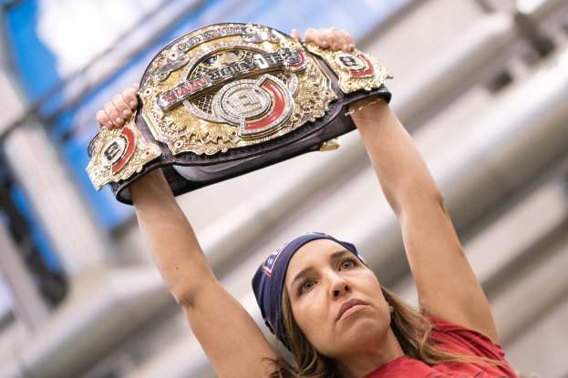 Frau in rotem T-Shirt und Headband, die eine Meisterschaftsmedaille vor ihrem Gesicht hält, mit einem unscharfen Hintergrund.
