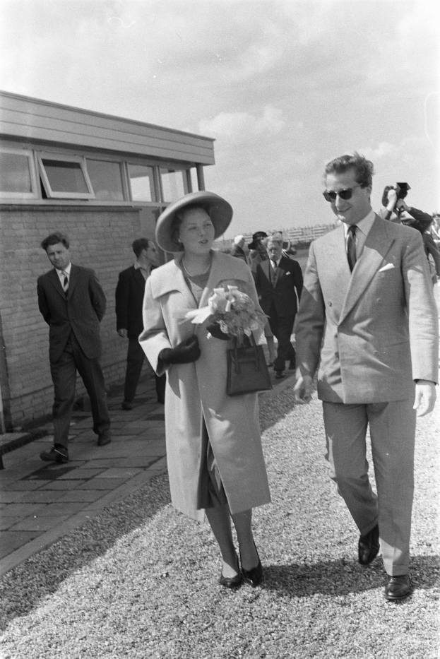 Königin Elizabeth II und Prinz Philip, Duke of Edinburgh, gehen zusammen, wobei die Queen einen Hut trägt und eine Handtasche hält, und der Duke eine Brille trägt, vor dem Hintergrund eines Gebäudes und eines bewölkten Himmels.