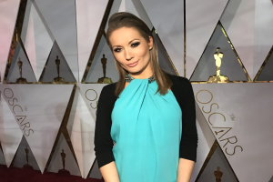 Frau in einem blauen und schwarzen Kleid auf dem roten Teppich der Oscar-Verleihung 2018, mit Skulpturen und Text im Hintergrund.