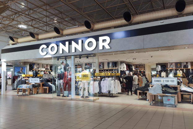 Ein Connor-Kleidungsgeschäft in einem Einkaufszentrum, das Schaufensterpuppen in aktueller Mode, Kleider an Bügeln, Texttafeln, Deckenleuchten und verschiedene andere Gegenstände zeigt.