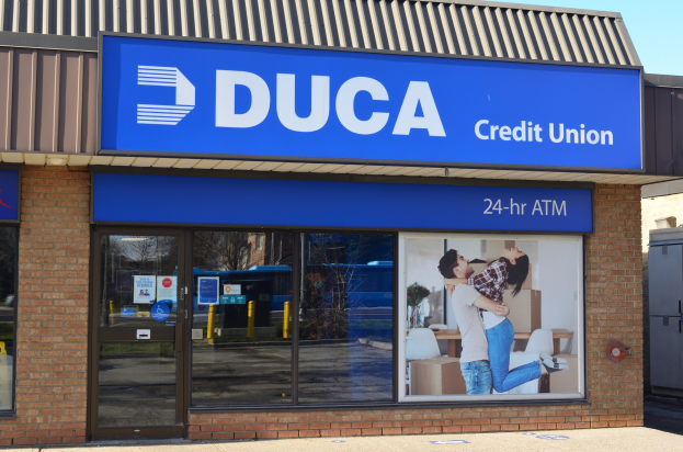 Außenansicht einer Duca Credit Union-Filiale mit Glaswänden, einem Schild mit einem Mann und einer Frau und einem Himmel als Hintergrund.