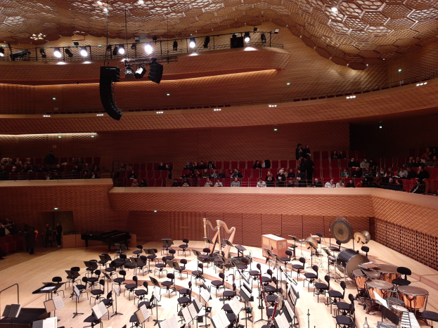 Großer Auditorium der Berliner Philharmoniker gefüllt mit Musikinstrumenten, Stühlen, Ständern und Menschen, mit beleuchteter Decke.