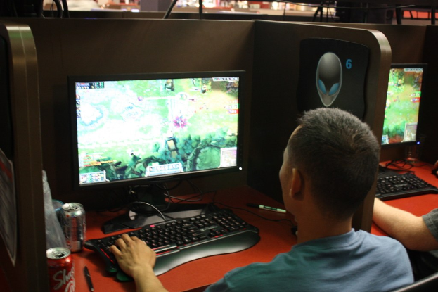 Personen an Tischen mit Computern und Softdrink-Dosen, scheinbar ein Spiel spielend.