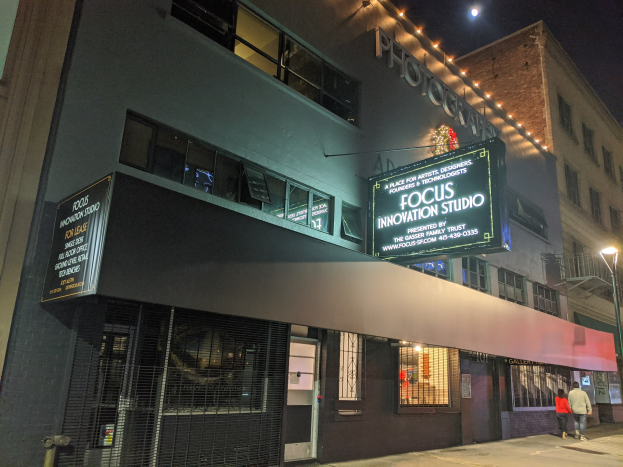 Außenansicht des Focus Innovation Studios in New York City bei Nacht, mit beleuchteten Gebäuden, Straßenlaternen, Passanten auf dem Bürgersteig und einem sichtbaren Nachthimmel.