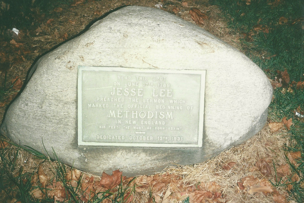 Ein großer Felsen mit einer Tafel, auf der "Jesse Lee Methodism" steht, umgeben von trockenem Laub und Gras.