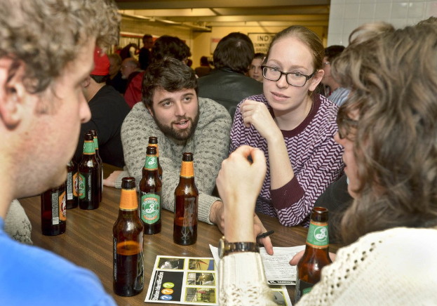 Menschen auf beiden Seiten eines Tisches mit Bierflaschen in einer Art Bar.
