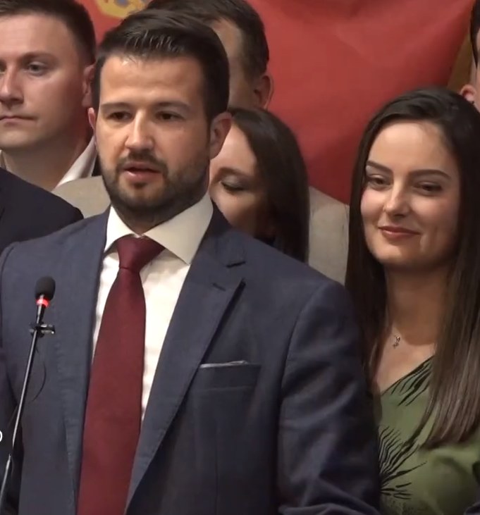 Ein Mann im Anzug spricht an einem Podium mit einem Mikrofon zu einer Menge hinter einem Banner, wahrscheinlich über ein Regierungsozialmedianverbot.