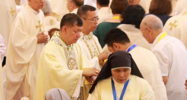 Eine Gruppe von Menschen in einer Kirche versammelt um eine Frau in Nonnenkleidung und einen Mann mit Brille.